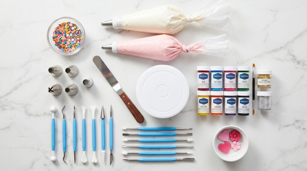 A flat-lay of essential cupcake decorating tools on a white marble surface